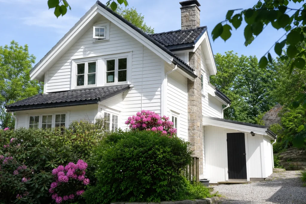 Fasade av en enebolig i Kristiansand med utvendig bod, rhododendron og synlig klebersteinspipe