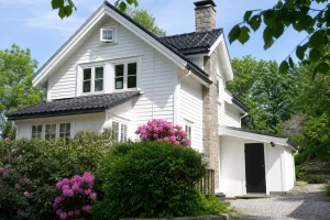 Fasade av en enebolig i Kristiansand med utvendig bod, rhododendron og synlig klebersteinspipe